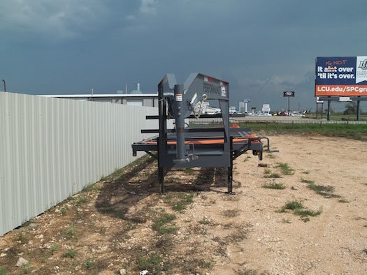 Trailer parked on a dirt lot with a fence and buildings in the background