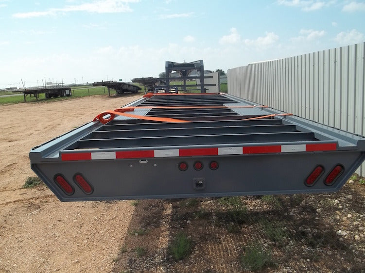 Flatbed trailer with orange straps on a dirt field under a blue sky.
