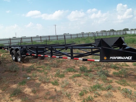 Black trailer with red and white stripes on a dirt field under a blue sky.