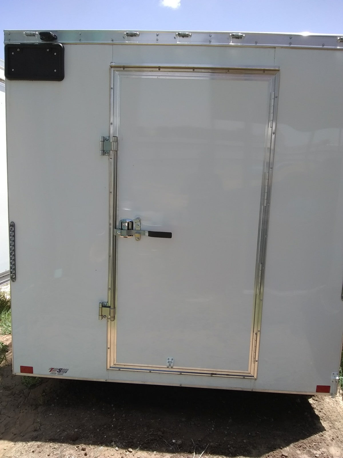 White trailer with a closed door on a dirt ground.