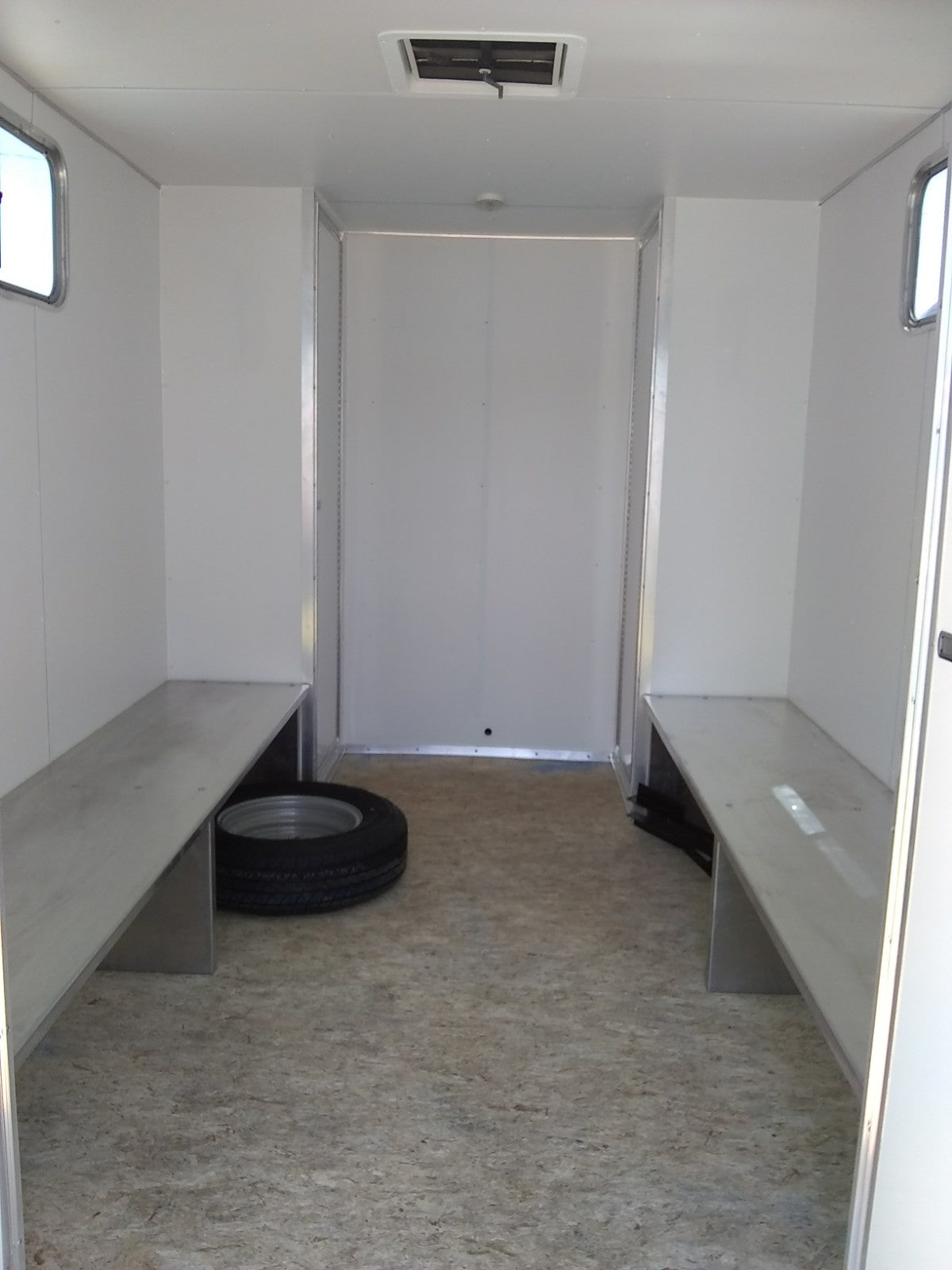 Small enclosed trailer with benches and a tire on a concrete floor