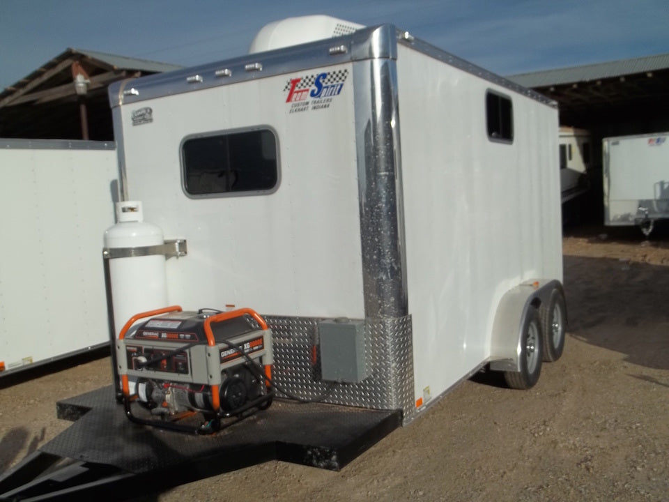 White enclosed trailer with a generator attached on a dirt surface.